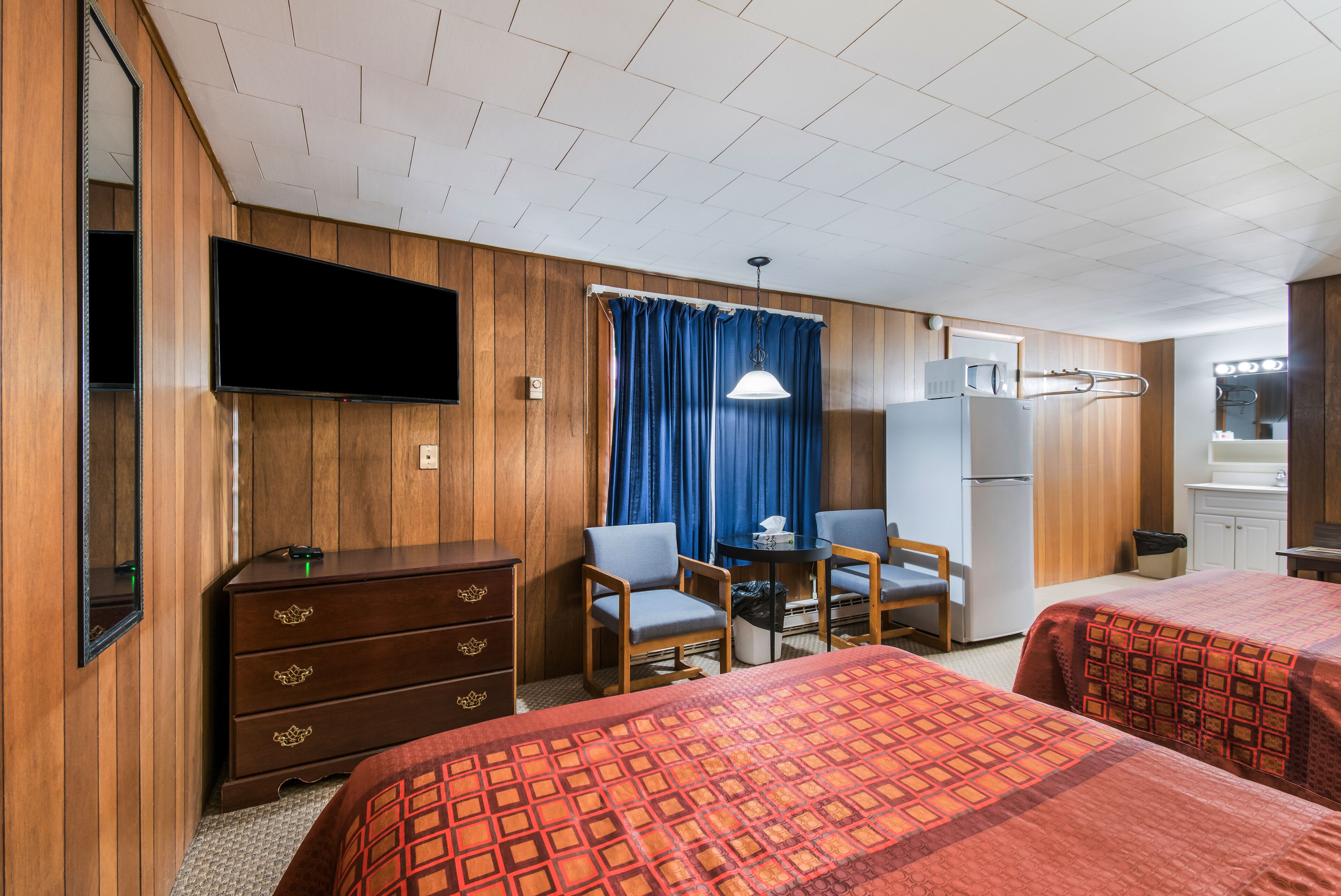 Een hotelkamer met twee bedden, een bureau, een stoel, een dressoir, een televisie en een kitchenette.