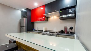 A modern kitchen with a glass island, stainless steel appliances, and red cabinetry. - Once21 Apartments (Guadalajara)