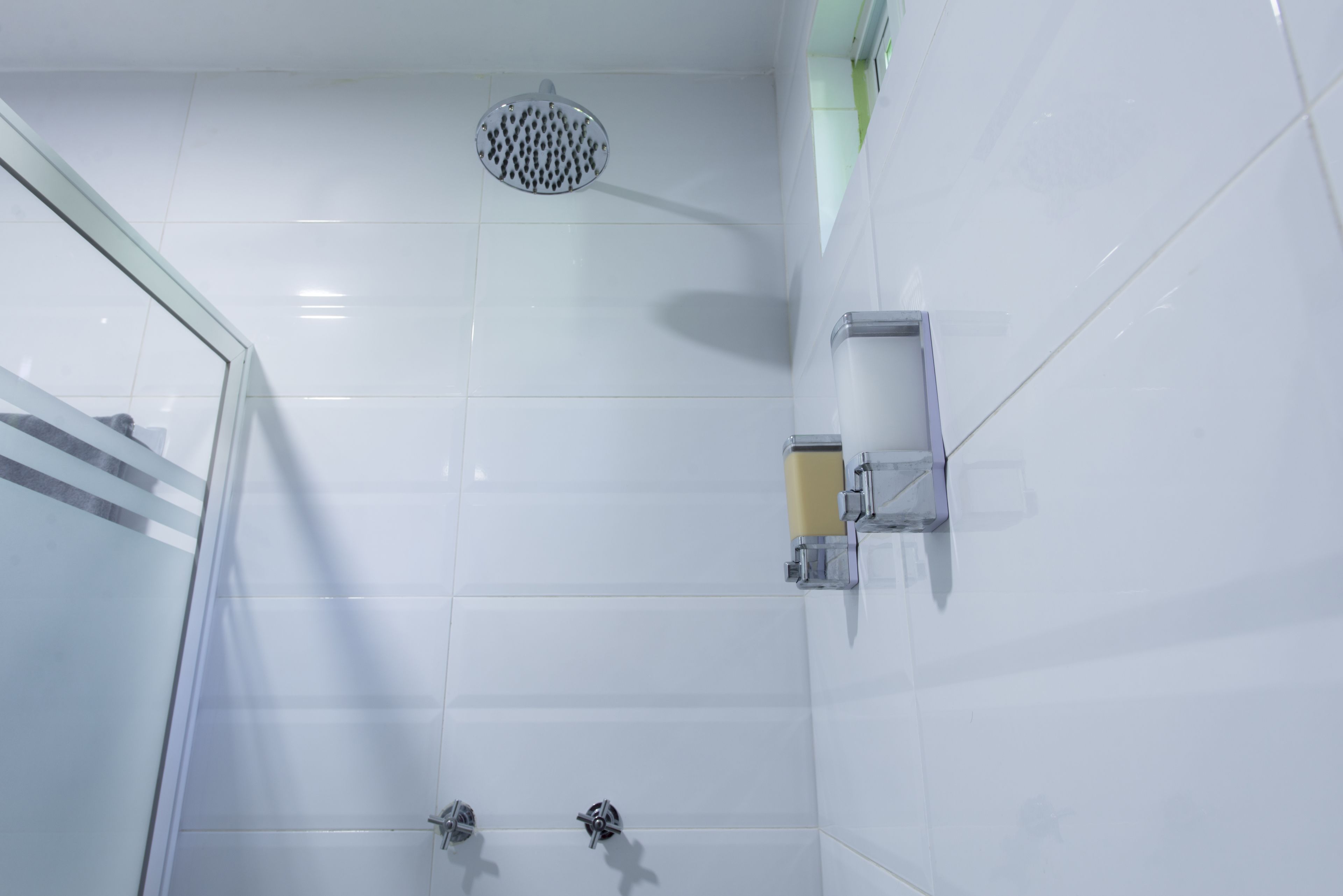 Une salle de bain moderne avec des carreaux blancs, une douche en verre et un distributeur de savon fixé au mur.