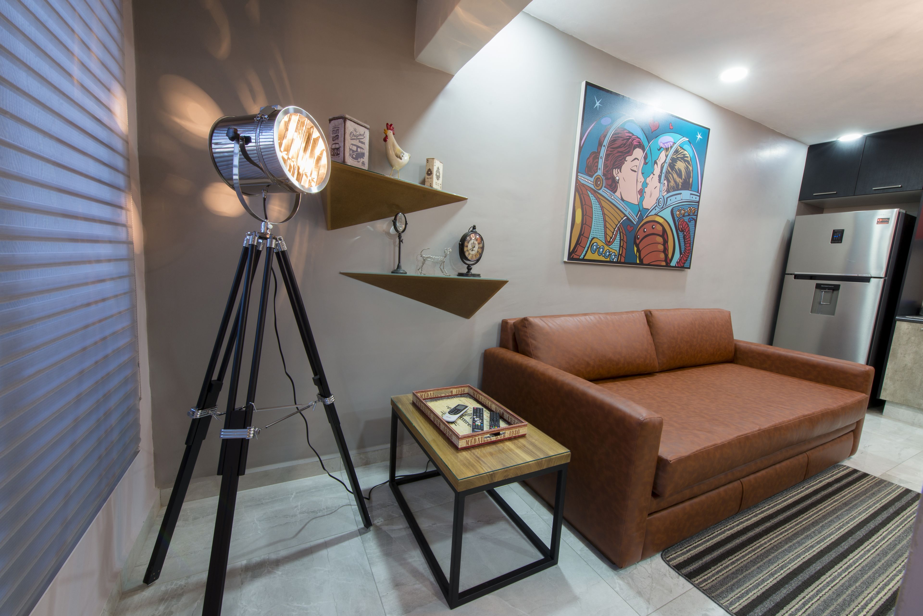 Una sala de estar con un sofá, una mesa de centro, una lámpara trípode y un cuadro en la pared.