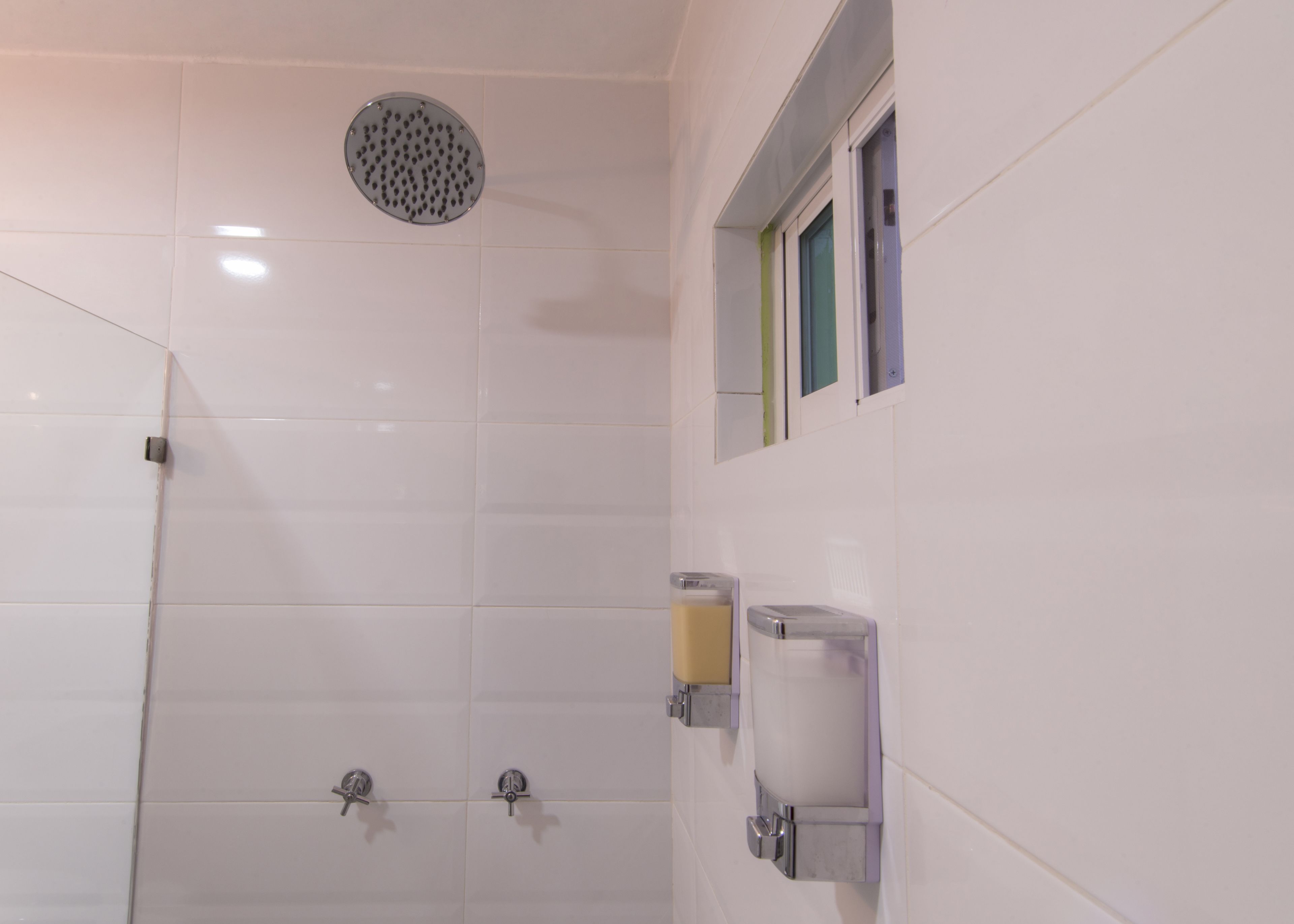 A bathroom with white tiles, a shower with a circular drain, and two faucets.