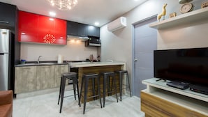 A modern kitchen with a red accent wall, a central island with bar stools, a built-in oven, and a flat-screen TV on a wooden stand. - Once21 Apartments (Guadalajara)