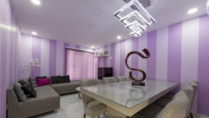 A modern living room with a glass-top dining table, grey sofas, and a large decorative letter 'S' on the wall. - Once21 Apartments (Guadalajara)