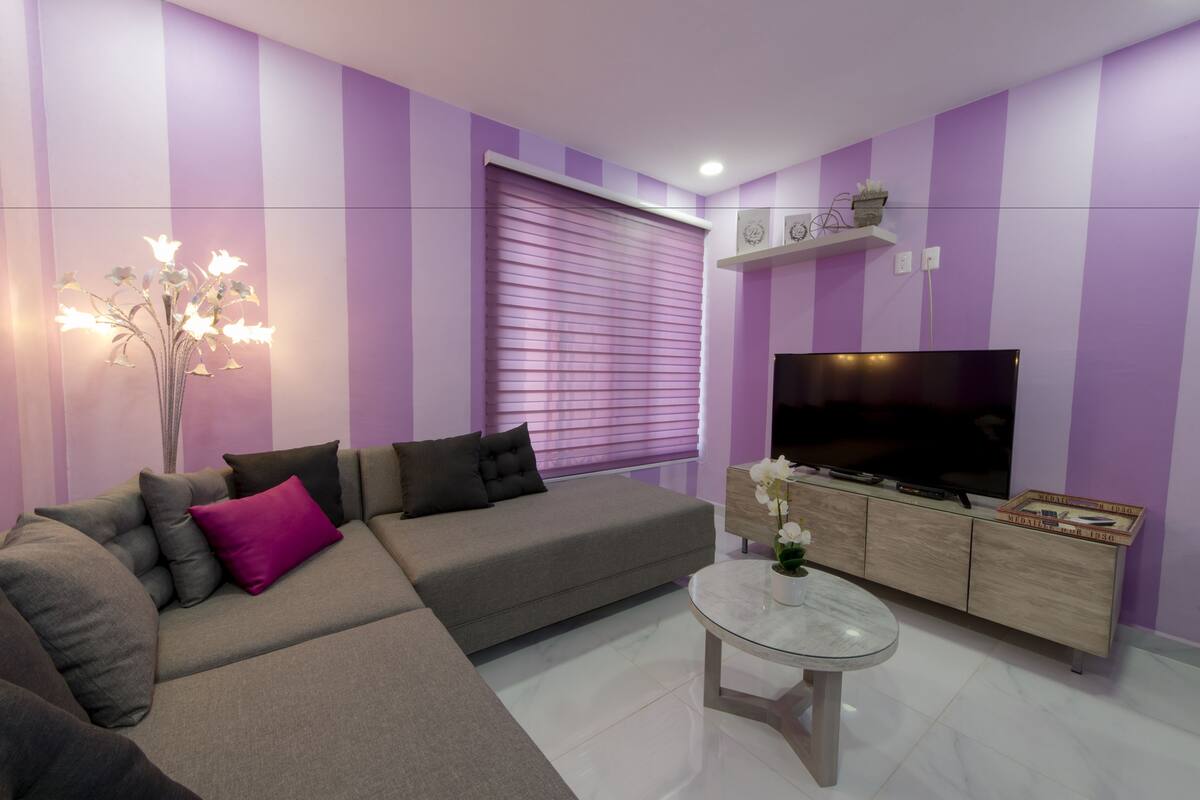 A modern living room with a grey sectional sofa, a glass coffee table, and a flat-screen TV on a wooden cabinet.