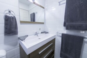 A bathroom with a white sink, a mirror, and two towels hanging on towel racks. - Once21 Apartments (Guadalajara)