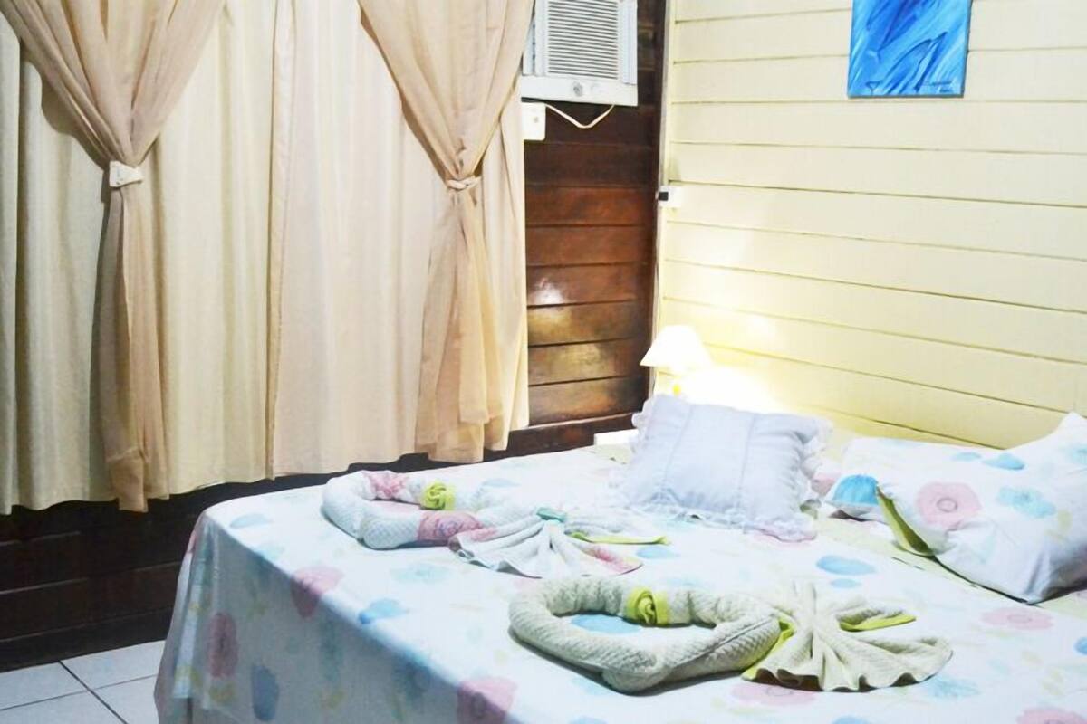 A bedroom with a bed covered in floral bedding, a bedside lamp, and a window with curtains.