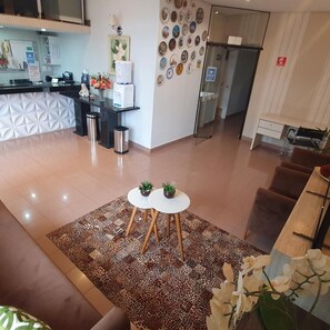 A hotel lobby with a reception desk, a patterned rug, and a seating area with two small tables. - Hotel Magnolia (Sao Joao da Boa Vista)
