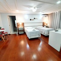 Quarto de hotel com duas camas, uma escrivaninha, uma cadeira e um ventilador de teto.