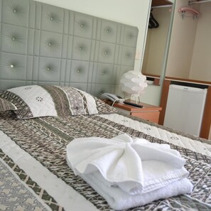 A hotel room with a tufted headboard, a patterned bedspread, a neatly folded white towel, a bedside telephone, and a mirror on the wall. - Hotel Magnolia (Sao Joao da Boa Vista)