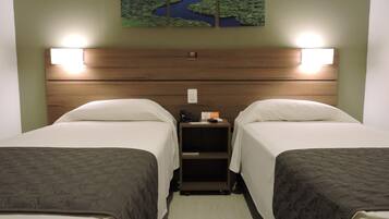 Een hotelkamer met twee bedden, een houten hoofdbord, bedlampjes, een nachtkastje met een telefoon en een bord, en een kunstwerk aan de muur van een landschap.