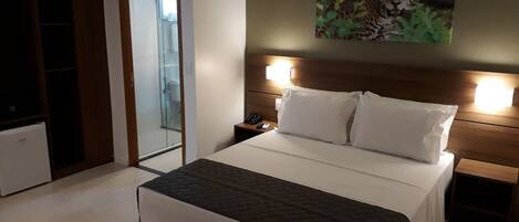 A modern hotel room with a large bed, a wooden headboard, a nightstand, a telephone, and a mirror.