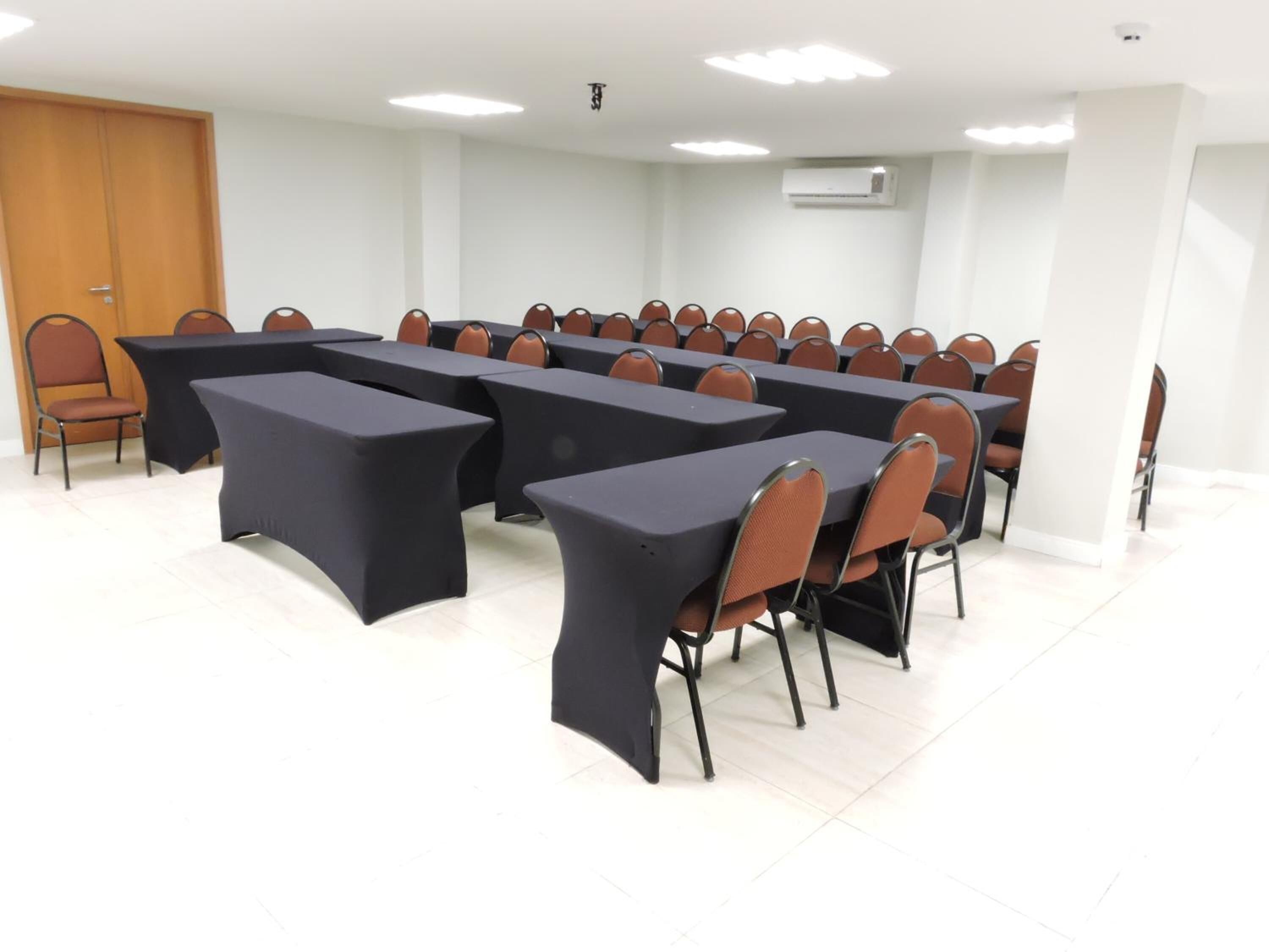 Une salle de conférence dotée de plusieurs tables et chaises, de murs blancs et d’un appareil de climatisation.