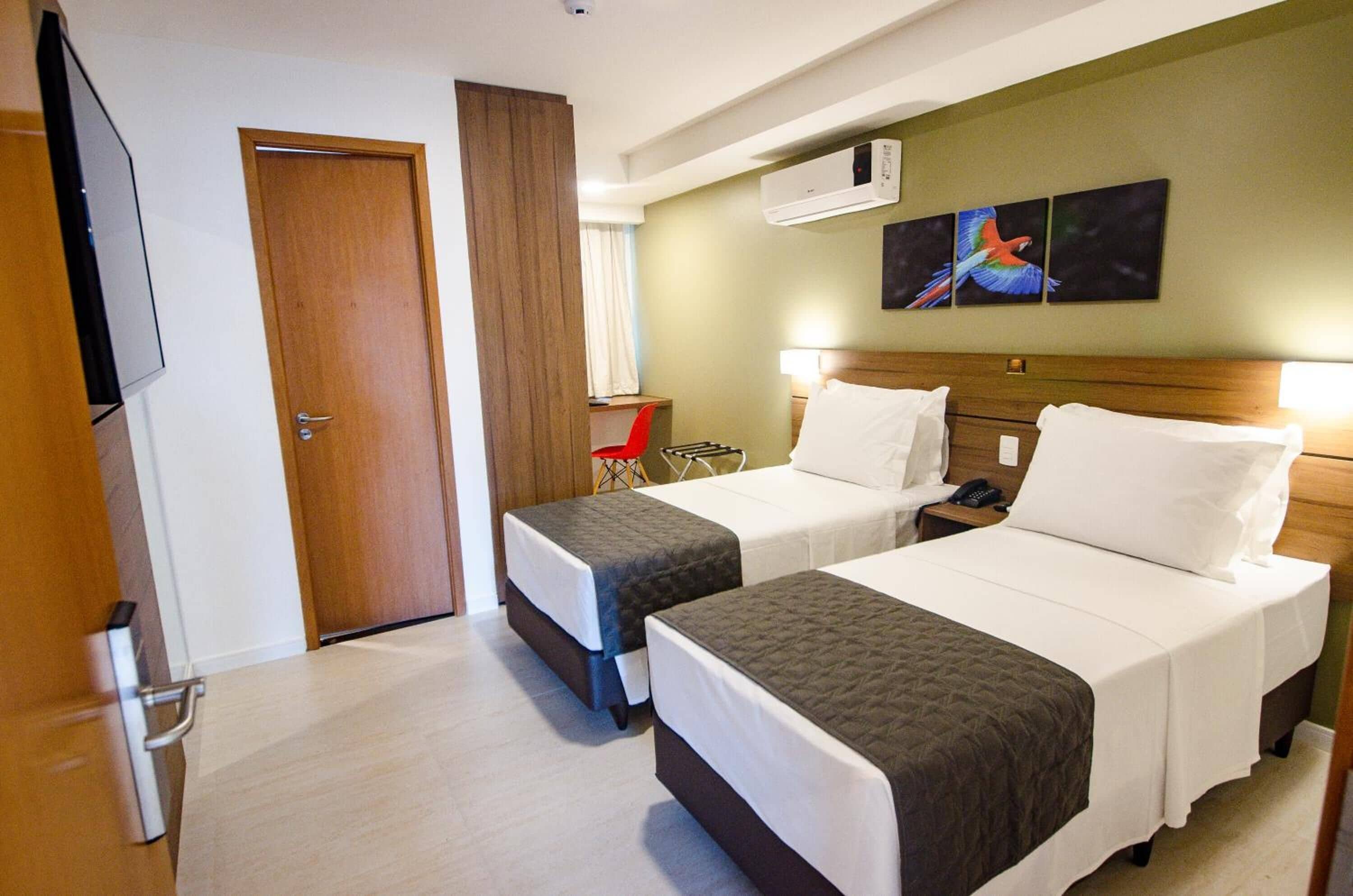 Una camera d'albergo con due letti, televisione, condizionatore e un quadro appeso al muro.
