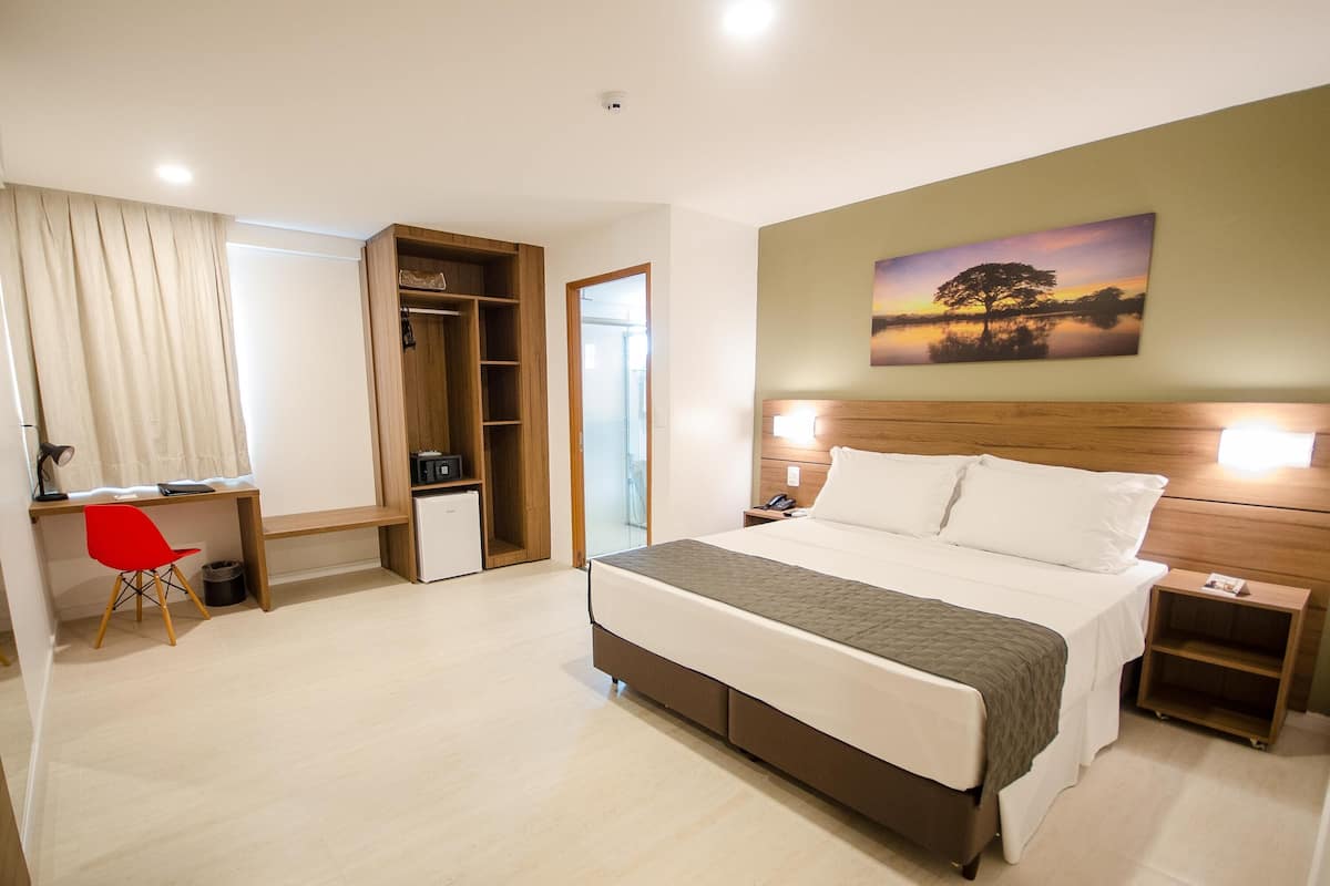 Una habitación de hotel con cama, mesitas de noche, escritorio, silla, armario y un cuadro en la pared.
