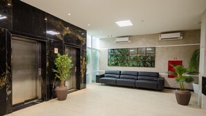 A modern lobby with two elevators, a sofa, potted plants, and a large window with a view of greenery. - Bristol Umarizal Belem (Belém)