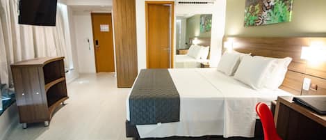 A hotel room with a bed, a desk, a chair, a TV, and a door.