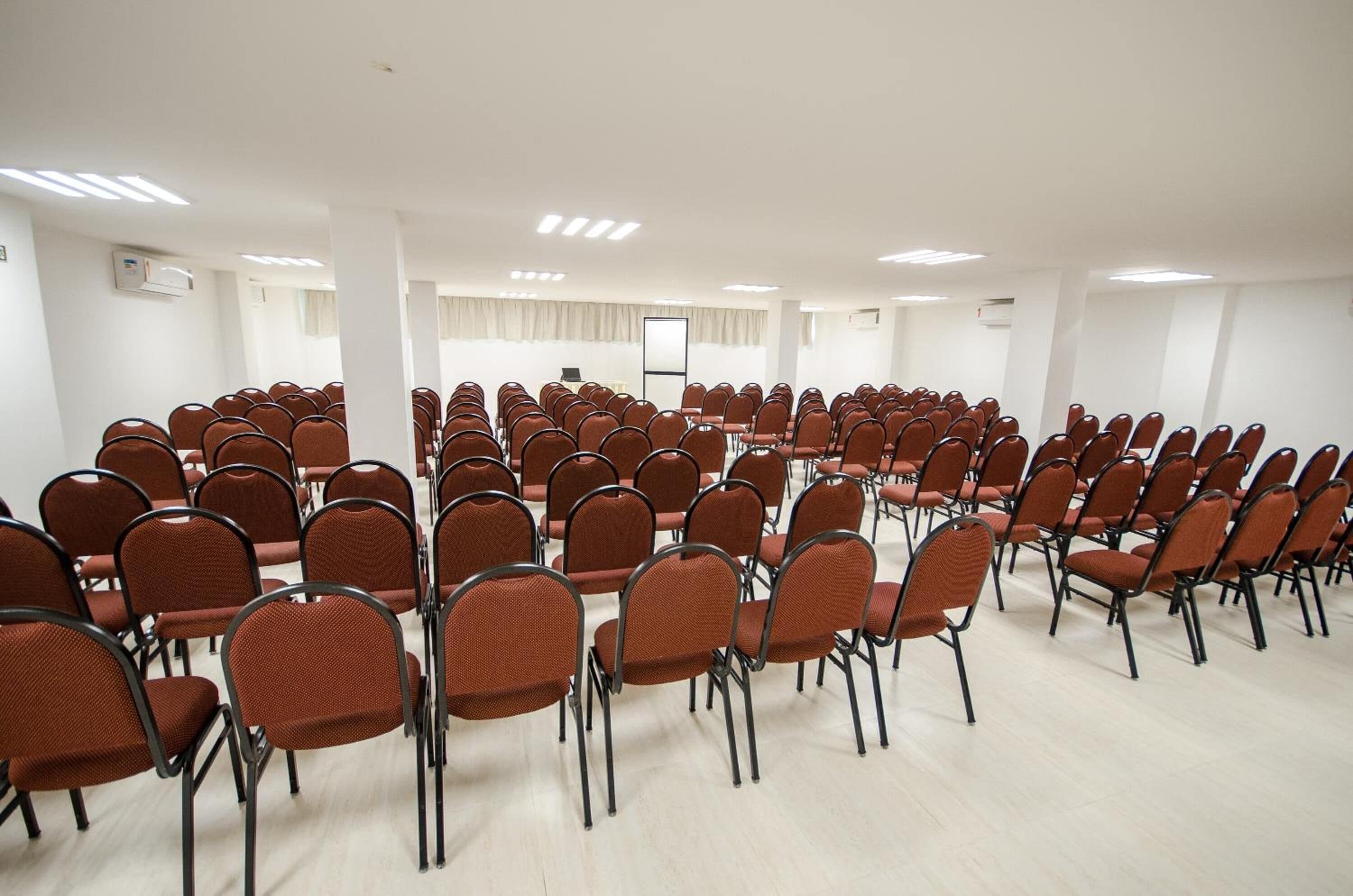 A conference room with rows of brown chairs, a whiteboard, and a projector screen.