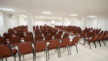 A conference room with rows of brown chairs, a whiteboard, and a projector screen.