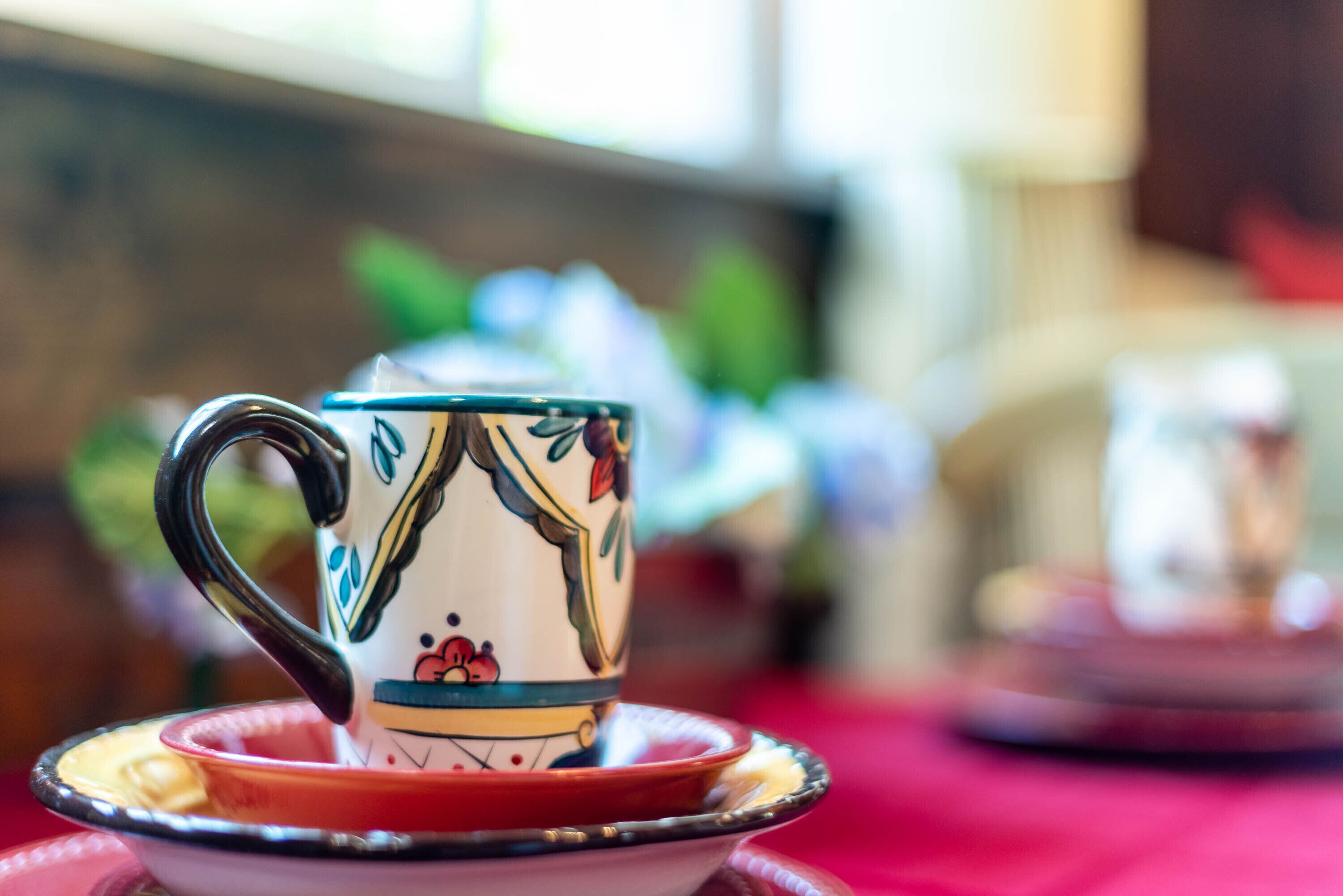 Een teacup met een bloemendecor op een schoteltje, geplaatst op een tafel met een rode tafelkleed.