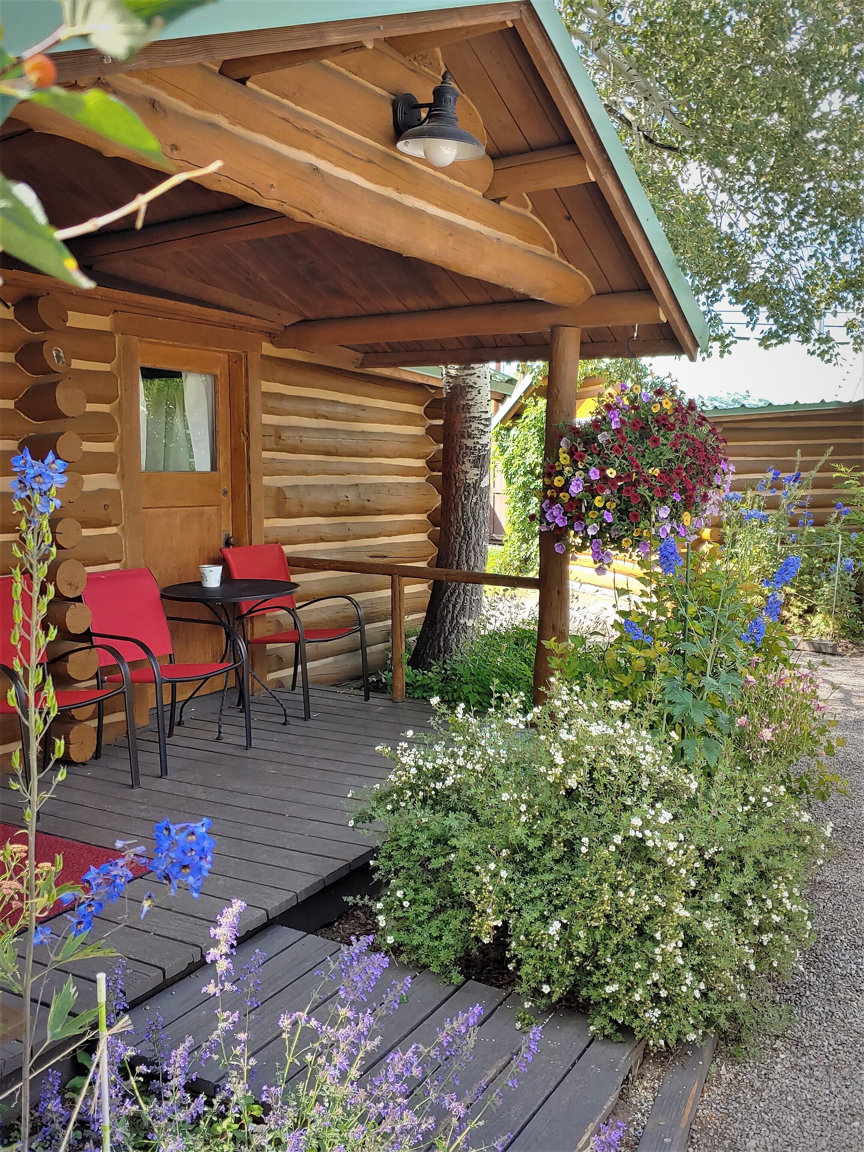 A log cabin with a porch, outdoor seating, and a hanging flower basket.