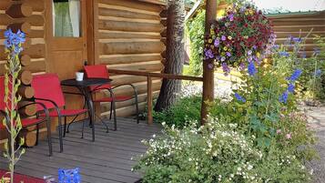 A log cabin with a porch, outdoor seating, and a hanging flower basket.