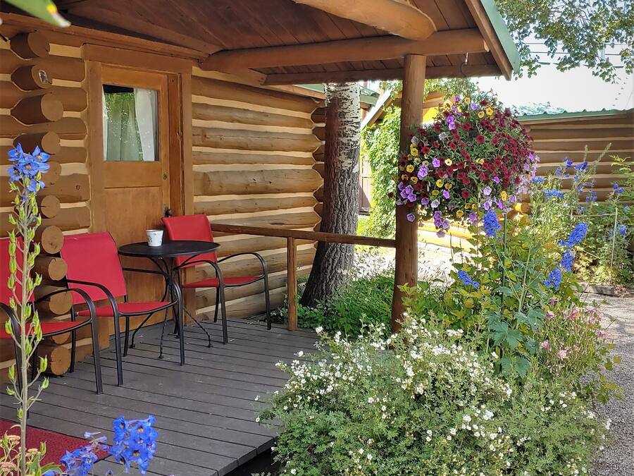 A log cabin with a porch, outdoor seating, and a hanging flower basket.