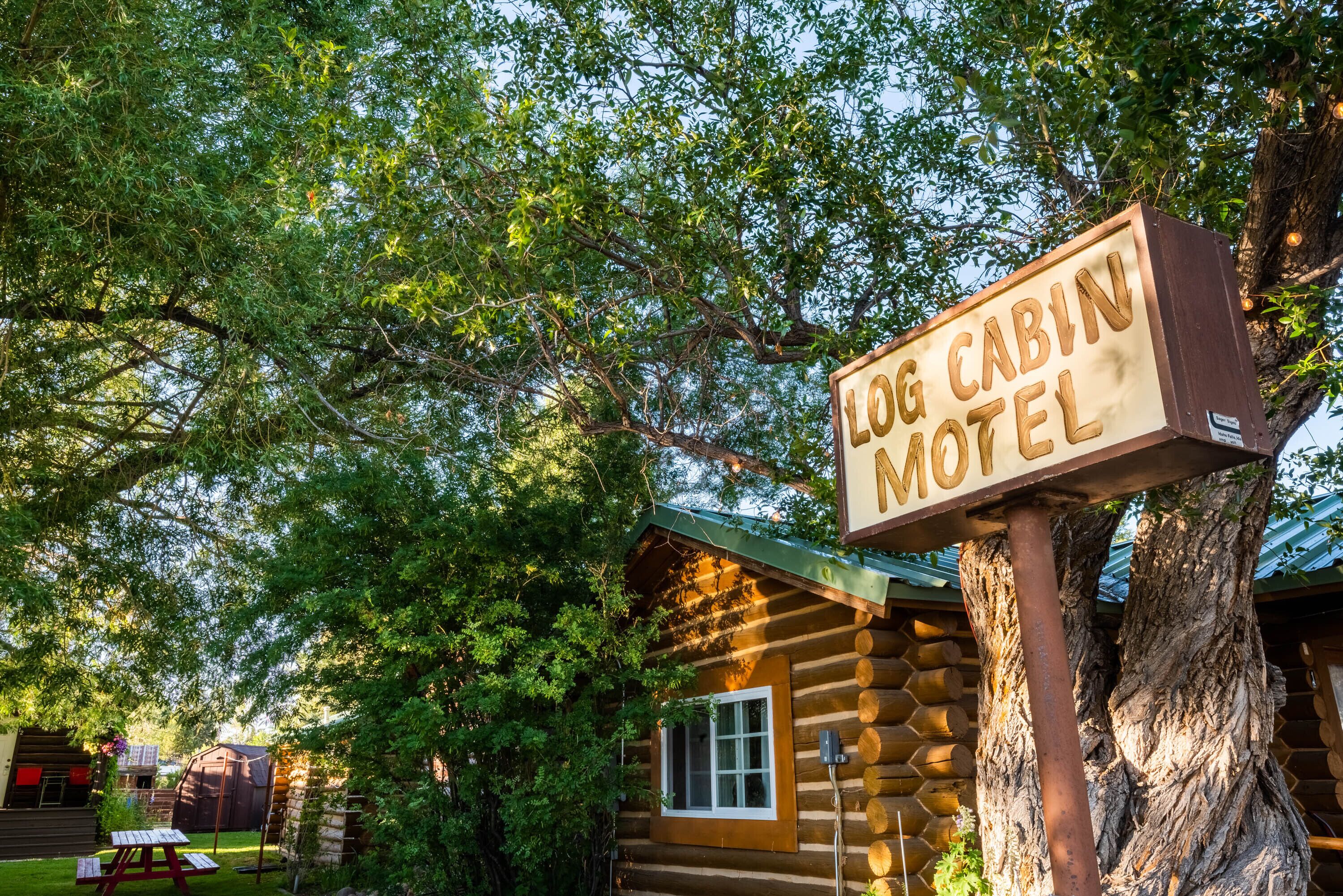 A log cabin motel with a wooden signboard, surrounded by lush greenery and trees.