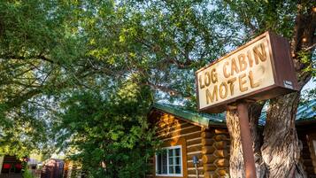 A log cabin motel with a wooden signboard, surrounded by lush greenery and trees.