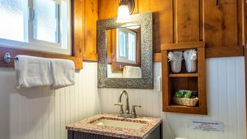 Une salle de bain avec un meuble-lavabo en bois, un évier surmonté d’un plan en marbre, un miroir avec un cadre orné et une étagère contenant des serviettes et des articles de toilette.