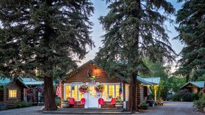 A log cabin with a 'Welcome Office' sign, red chairs, and American flags. - Log Cabin Motel (Pinedale)