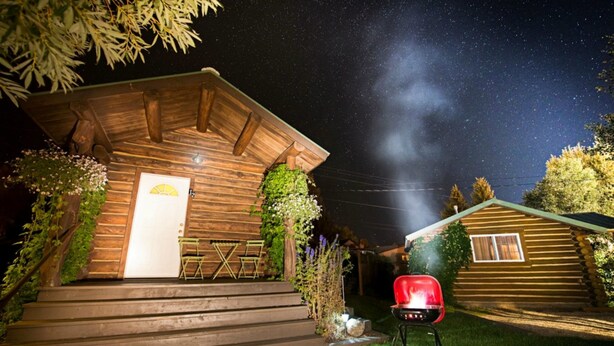 A wooden cabin with a porch, a grill, and a starry night sky. - Log Cabin Motel (Pinedale)