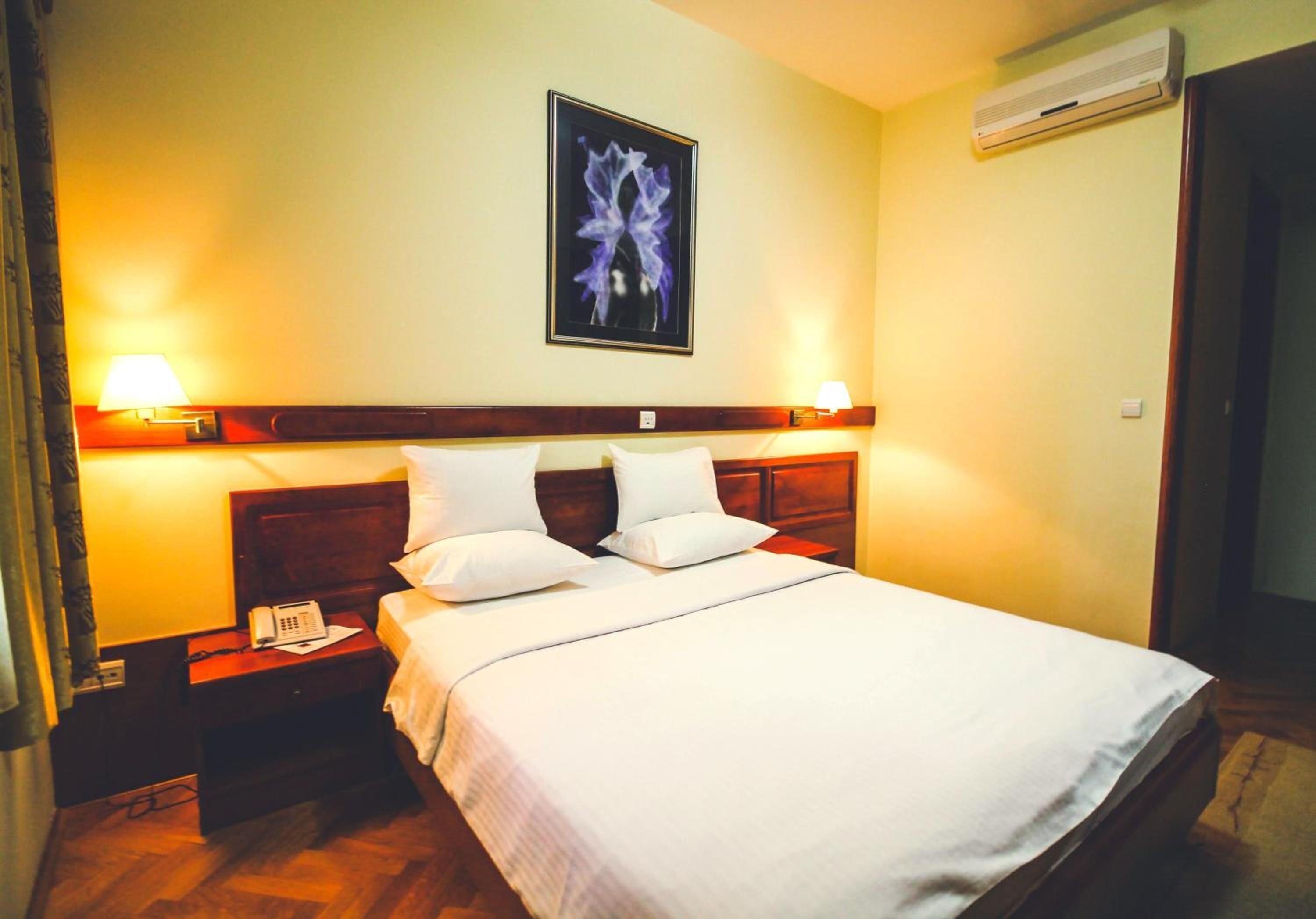 A hotel room with a bed, two bedside lamps, a telephone, and a framed picture on the wall.