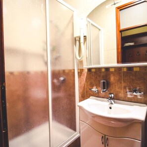 A bathroom with a glass shower enclosure, a sink with a mirror, and a wooden cabinet. - Vila Vrbas (Banja Luka)