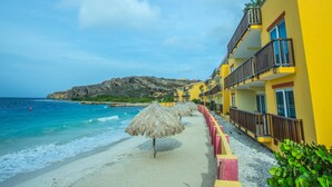 A beachside hotel with a clear view of the ocean, a sandy beach, and a rocky hillside in the background. - Palapa Beach Resort (Jan Thiel)