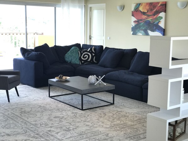 Una sala de estar moderna con un sofá seccional azul oscuro, una mesa de centro de vidrio y un estante blanco.