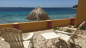 A beachside seating area with two white plastic chairs and a thatched umbrella, overlooking a clear blue sea. - Palapa Beach Resort (Jan Thiel)