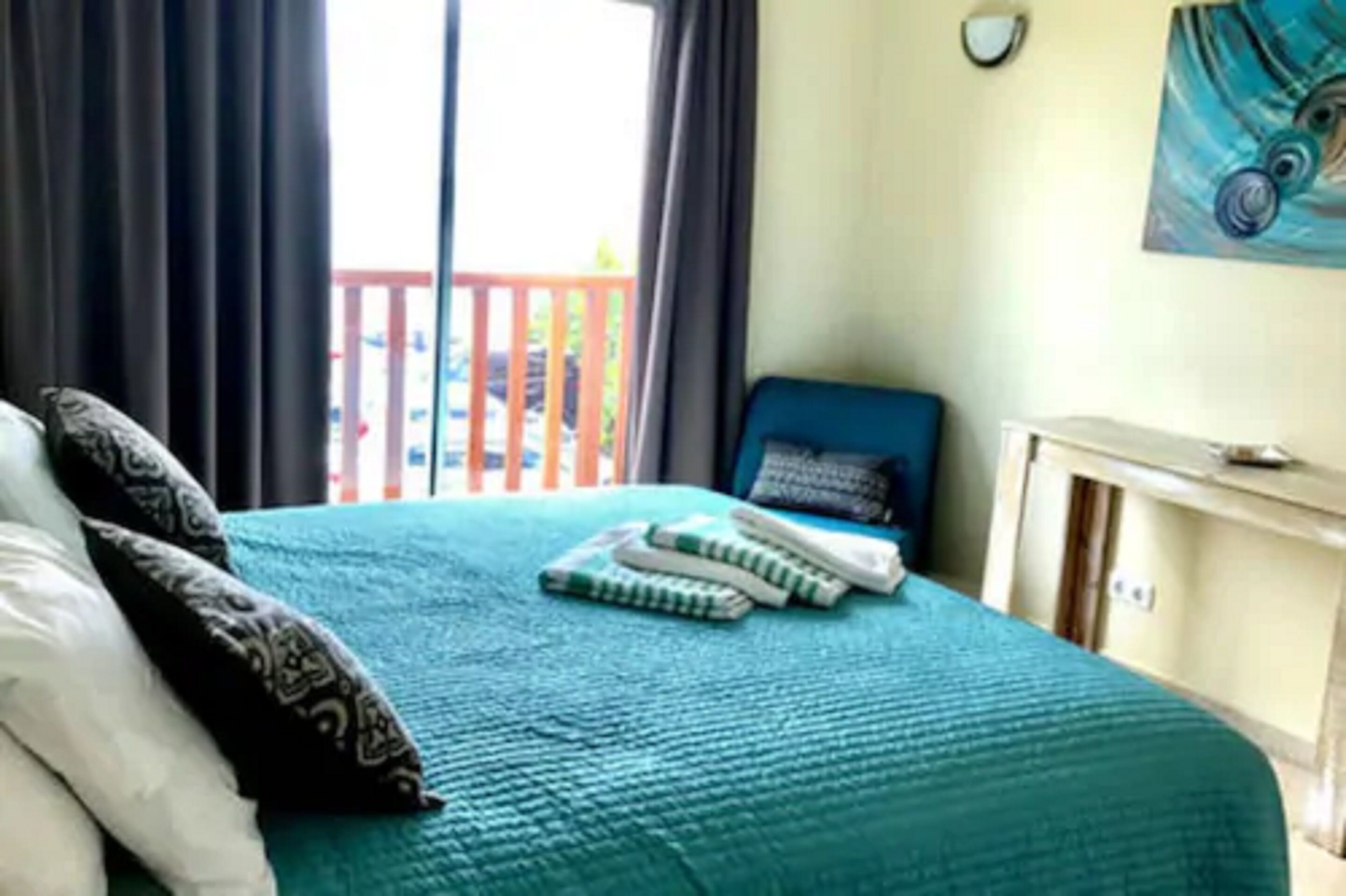 Un dormitorio con cama, almohadas, una mesita de noche, un cuadro y vistas a un balcón.