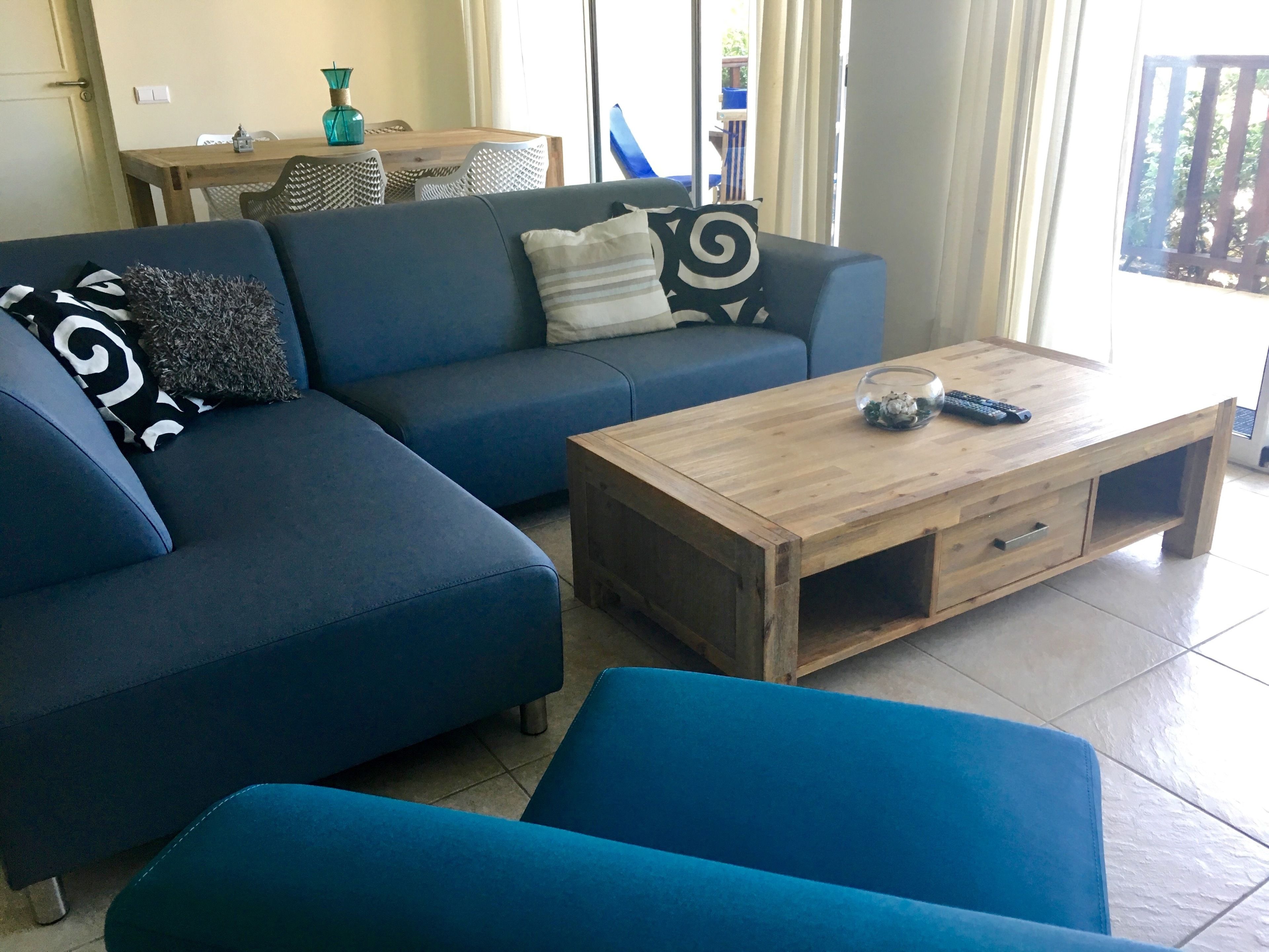 Een woonkamer met een blauwe bank, een houten salontafel en een eethoek met een tafel en stoelen.