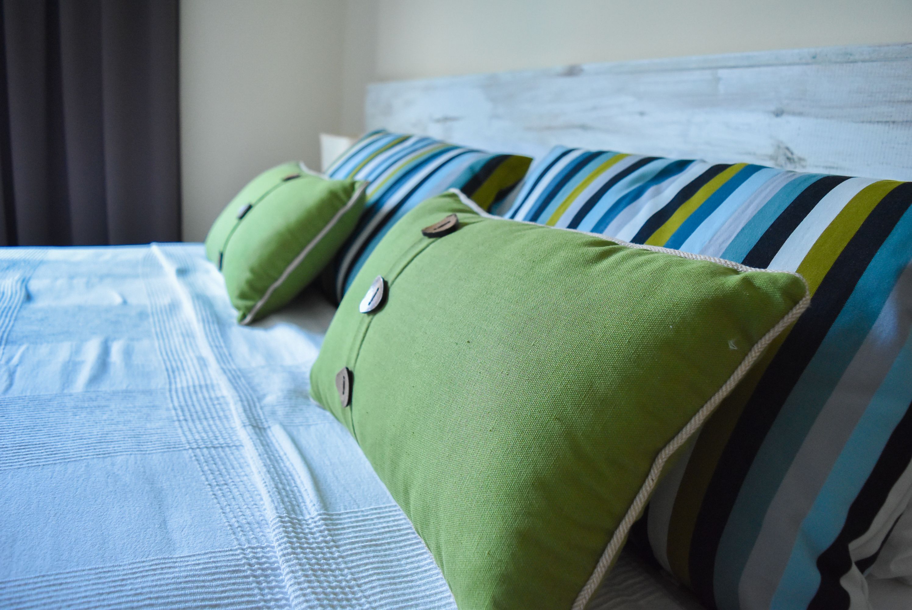 Ein Bett mit einem gestreiften Kopfkissen und einem grünen Kopfkissen mit Knöpfen.