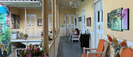 A covered outdoor area with a seating arrangement, a person reading, and a mural on the wall.