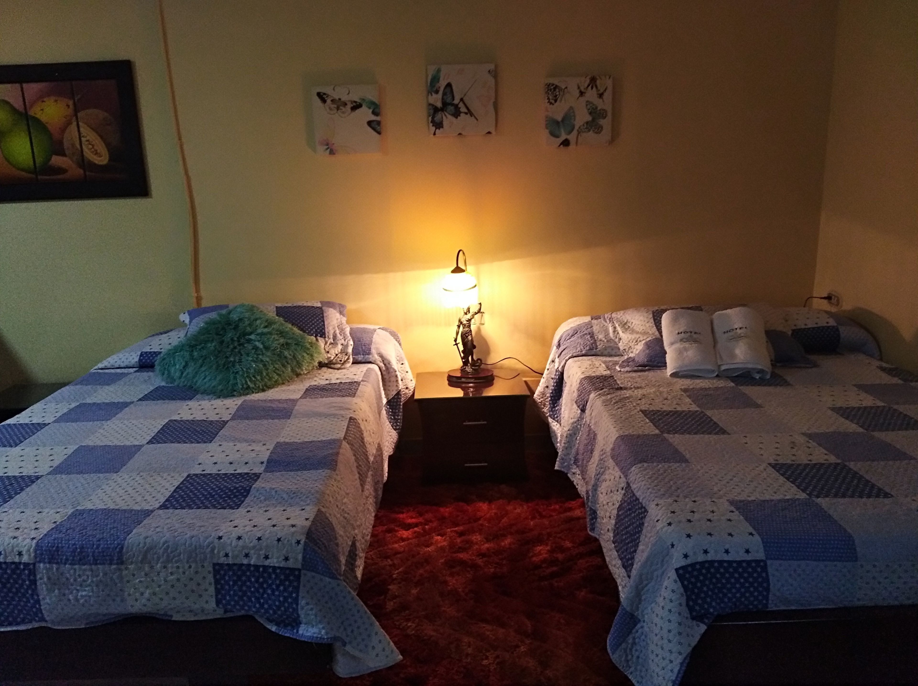 Ein Zimmer mit zwei Betten, jeweils mit einer blau-weißen Steppdecke, einem kleinen Tisch mit Lampe und einem roten Teppich.