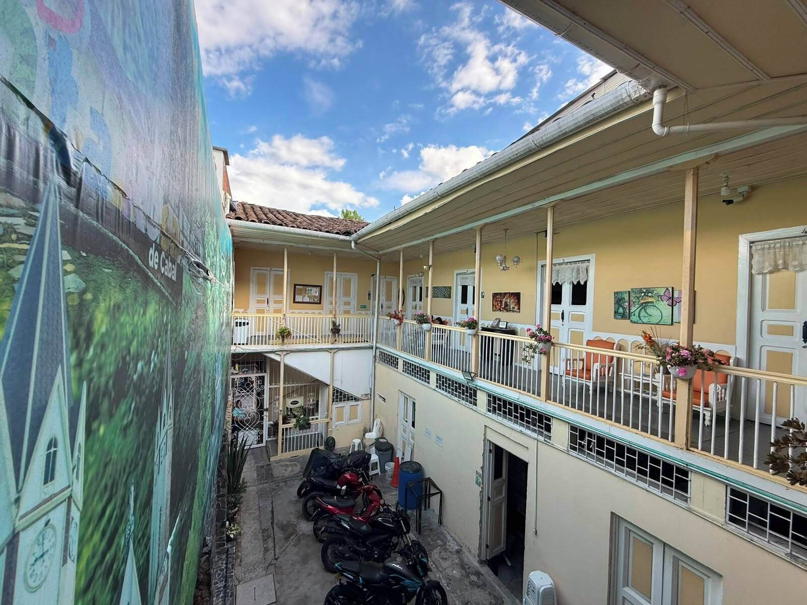 Un edificio de varios pisos con balcones, un espacio al aire libre cubierto y motocicletas estacionadas.