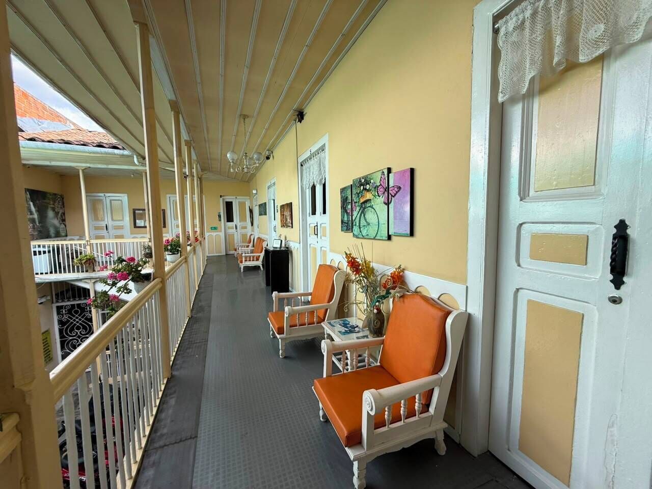 A corridor with a balcony, wicker chairs, a door, and artwork on the wall.