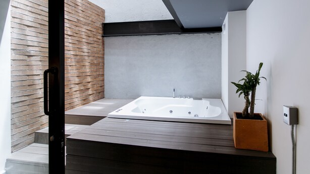 A modern bathroom with a wooden floor, a white bathtub, and a potted plant. - Soy Local Provenza (Medellín)