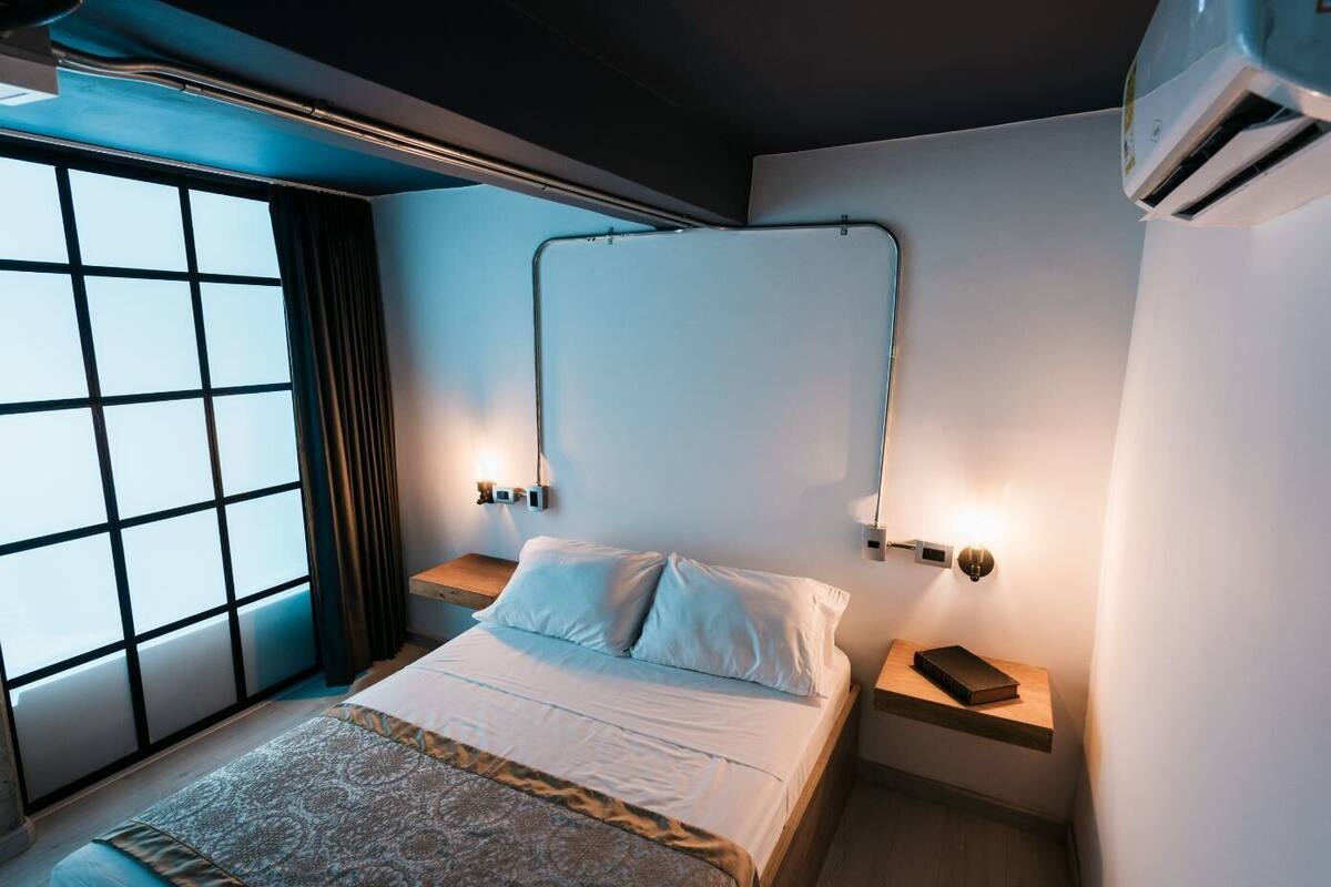 Un dormitorio moderno con una cama grande, dos mesitas de noche, una ventana con cortinas y un equipo de aire acondicionado.