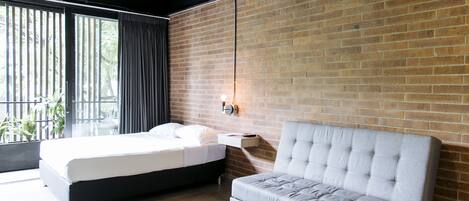 Un dormitorio moderno con cama, sofá, una mesa de centro de madera y una pared de ladrillo.
