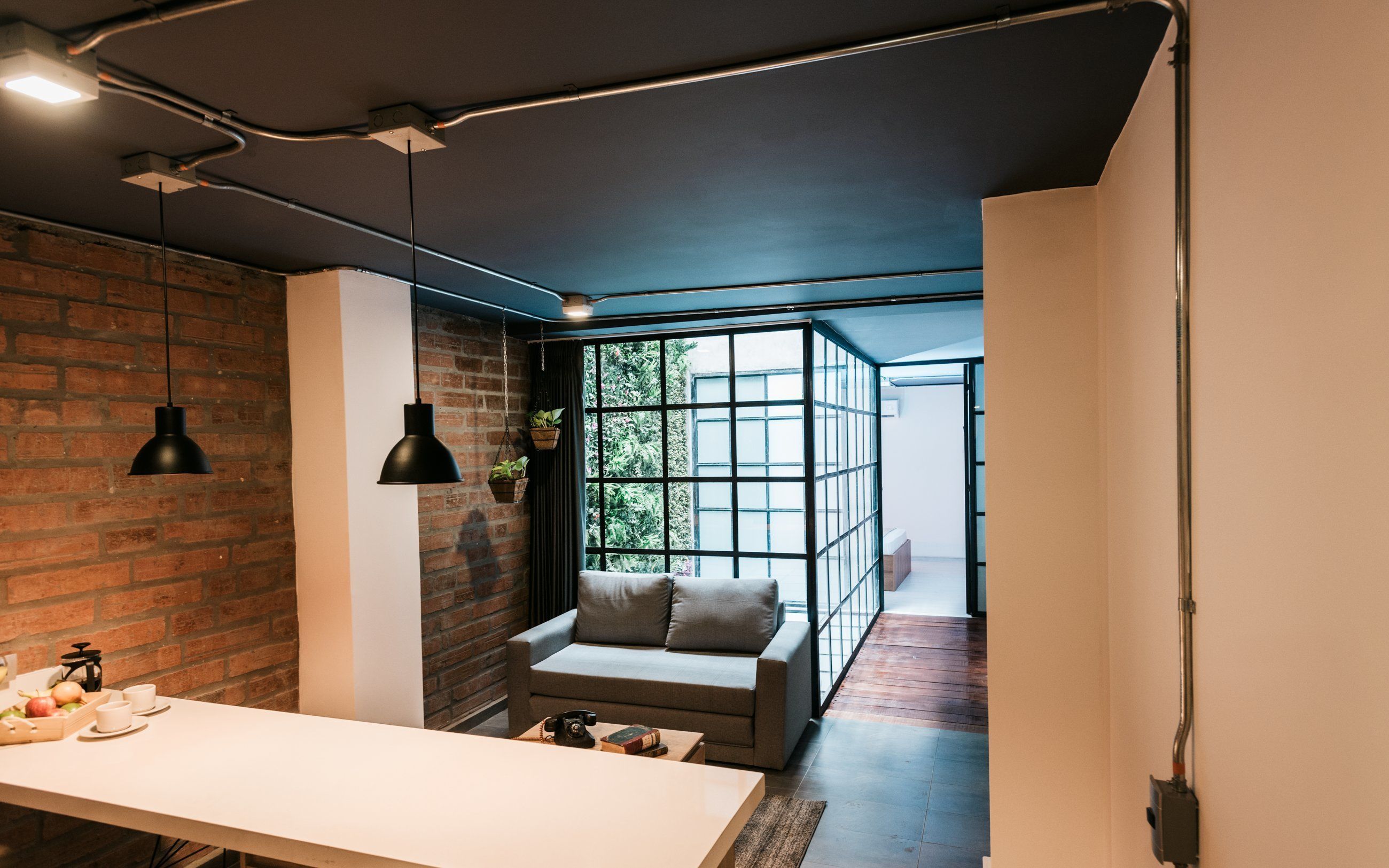 Um interior moderno com parede de tijolos, sofá, mesa e plantas penduradas.