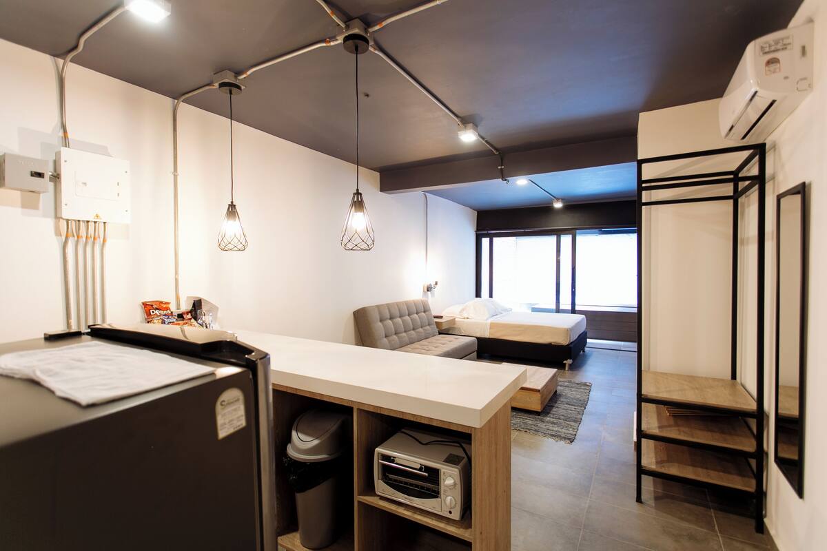 Una habitación moderna y luminosa con kitchenette, un sofá y una cama.