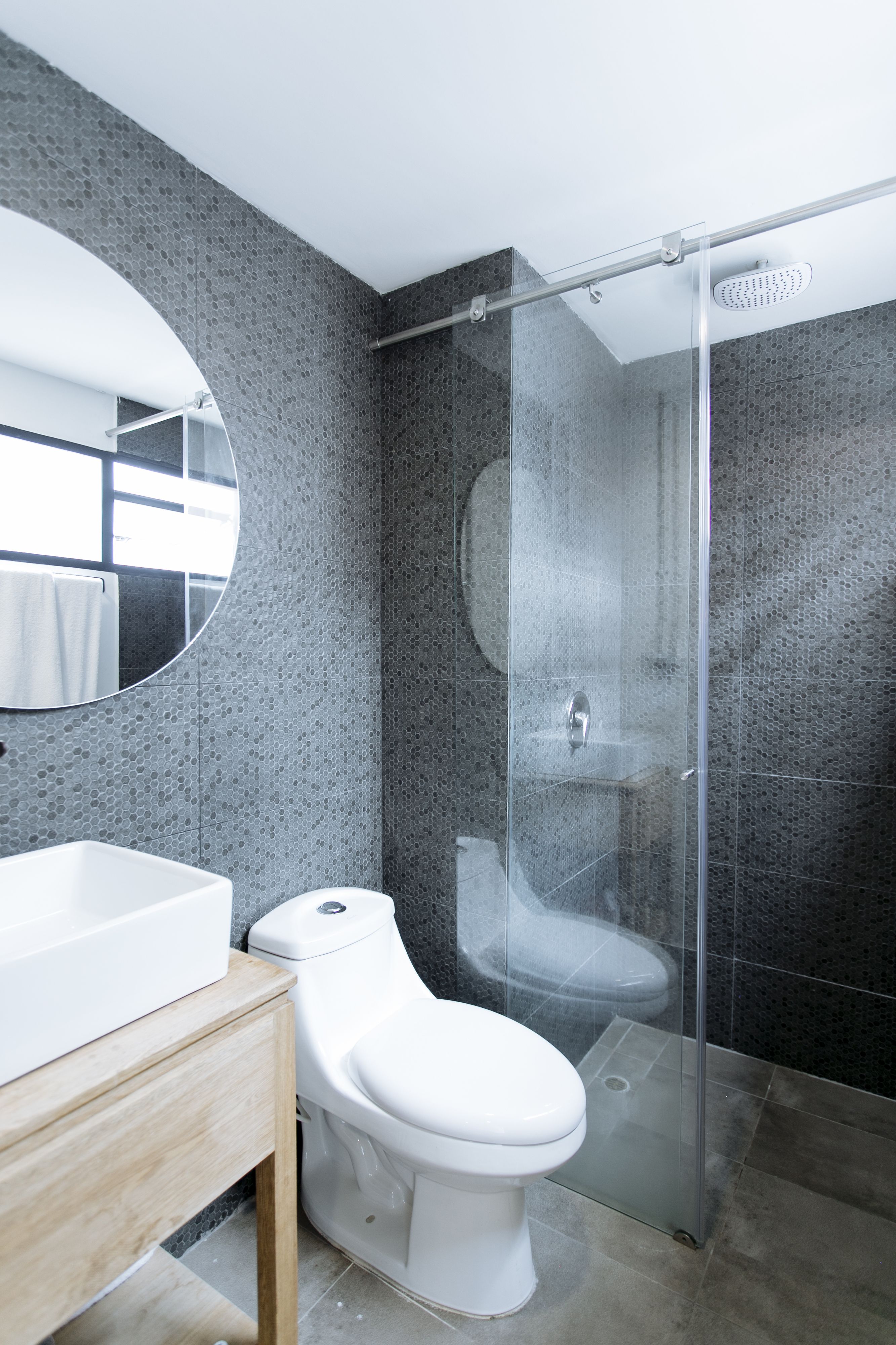 A modern bathroom with a glass-enclosed shower, a white toilet, and a wooden vanity.