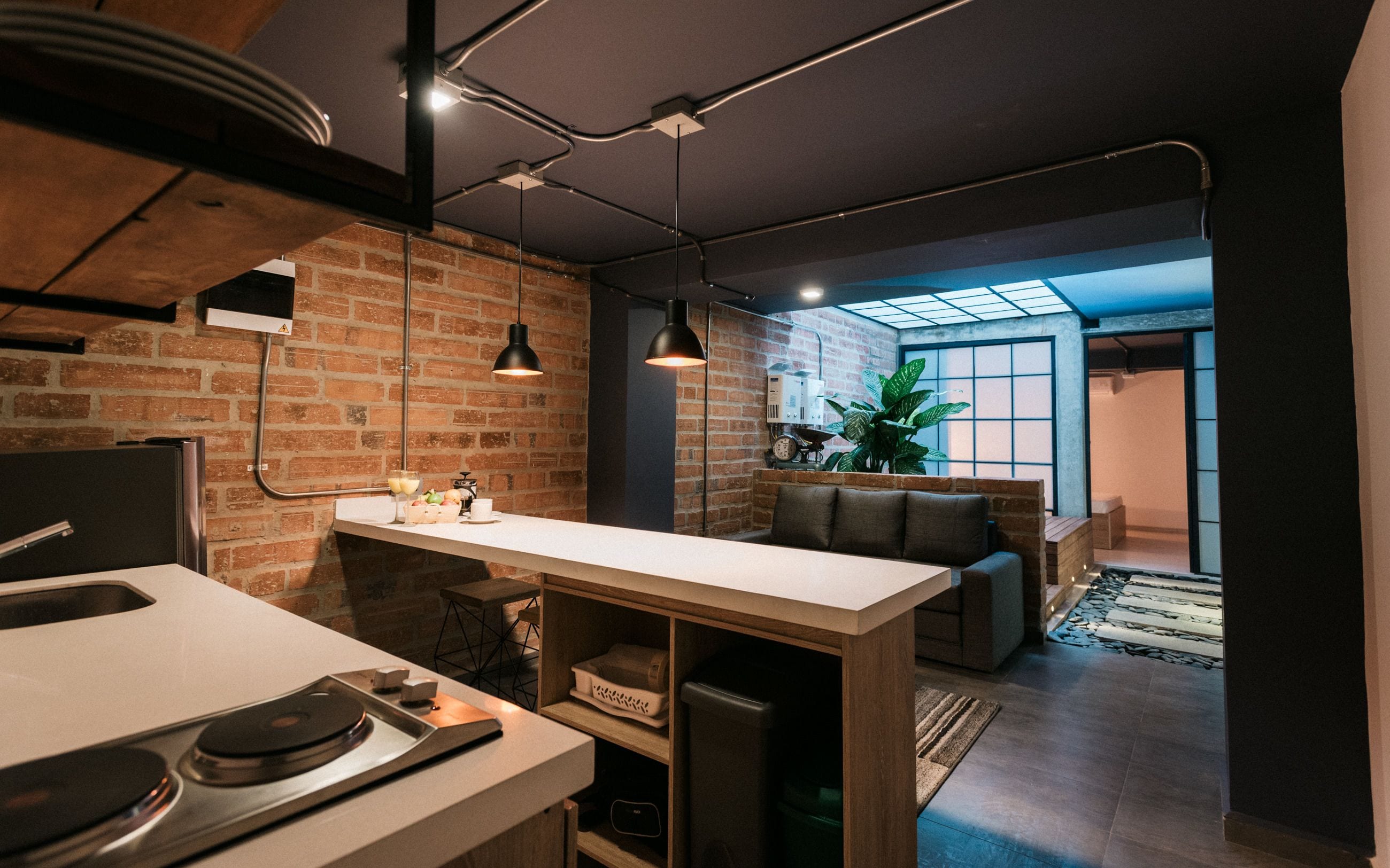 A modern kitchen with a brick wall, a dining area with a bench, and a view of a cityscape through large windows.